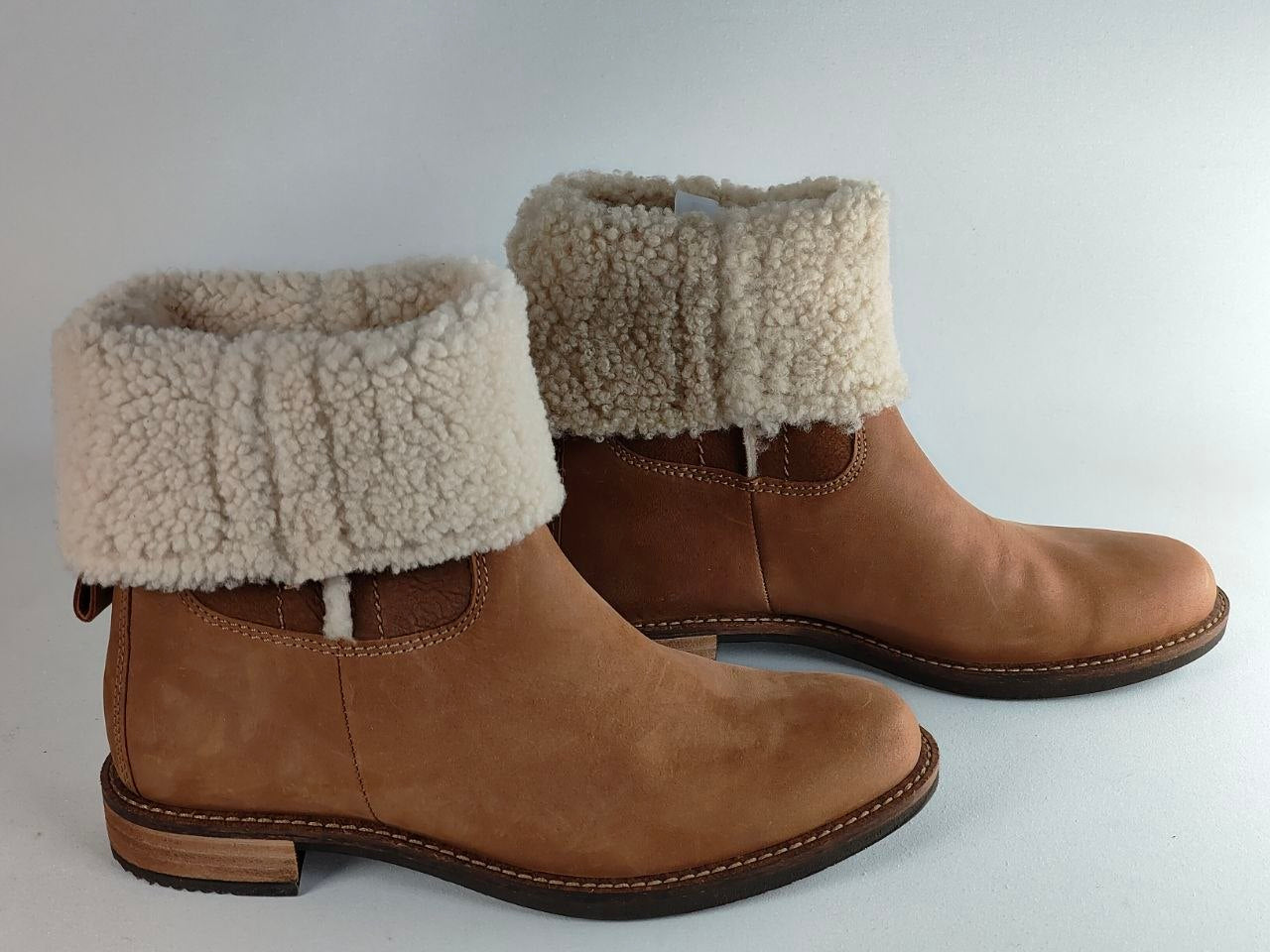 A pair of women's ankle boots in tan suede with a thick, fluffy cream sherpa fleece cuff, shown against a neutral light gray background.