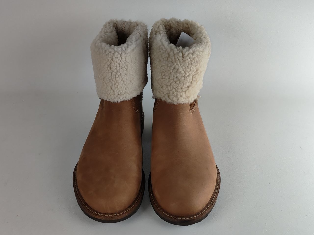 A pair of tan suede ankle boots with thick cream shearling-style fleece cuffs, photographed from the front on a light gray background.