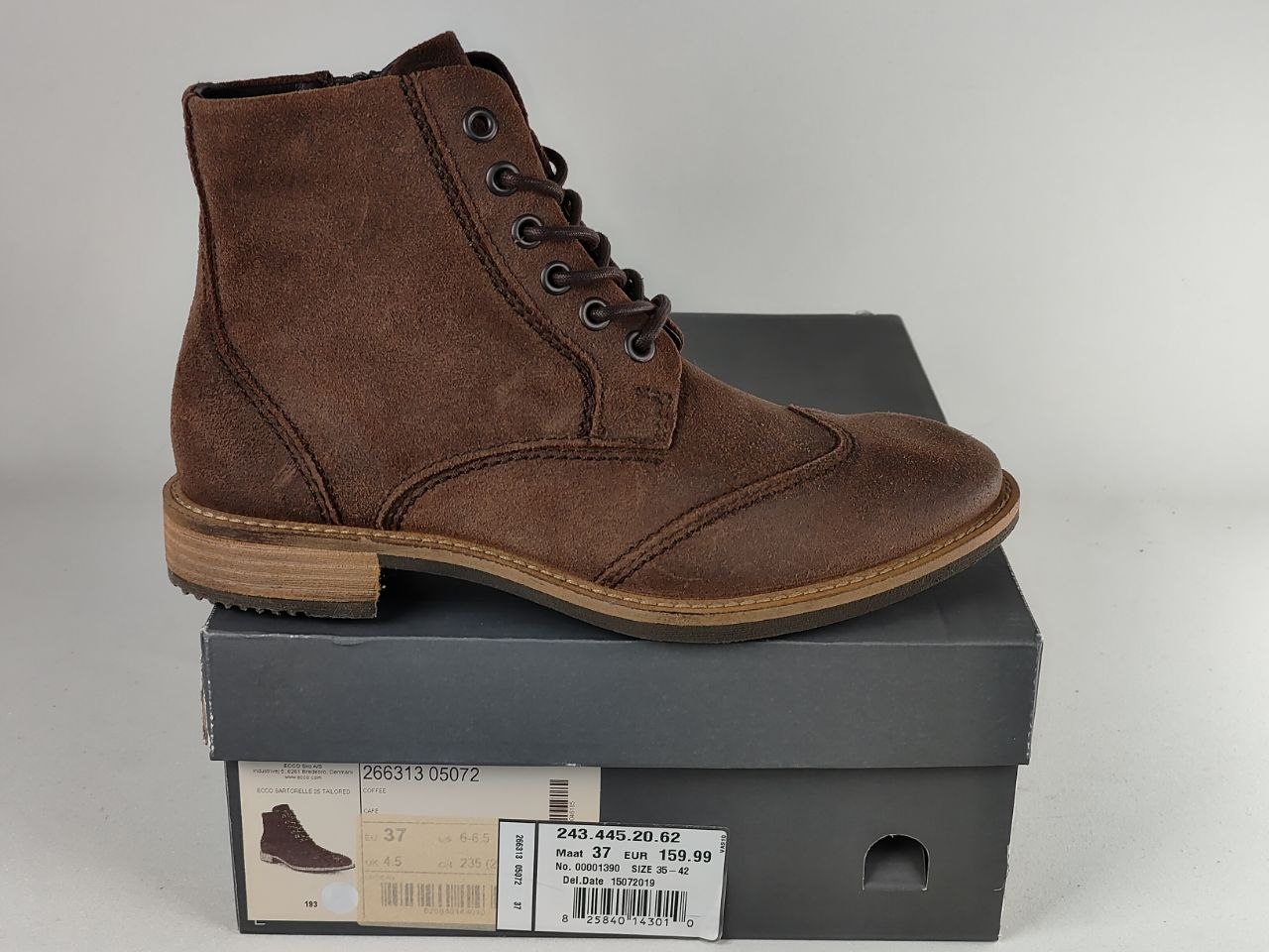 A brown suede lace-up ankle boot displayed on top of a dark gray shoebox against a light gray background.
