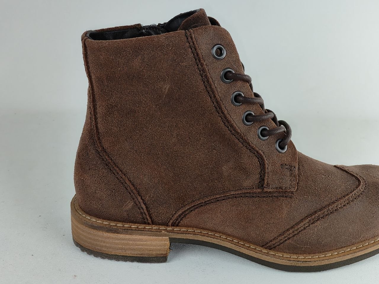 A brown suede lace-up ankle boot with a low stacked heel and metal eyelets, shown from a side profile view against a light gray background.