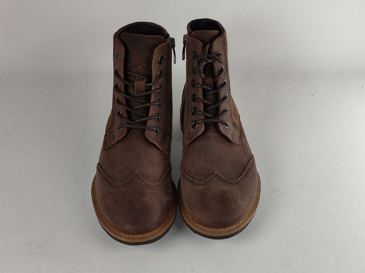 A pair of dark brown suede lace-up ankle boots with side zippers, shown from the front on a neutral light gray background.