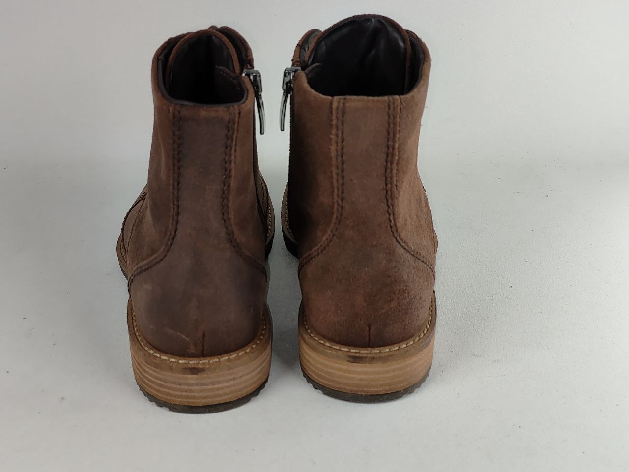 A pair of dark brown suede ankle boots with side zippers and stacked wood-look soles, shown from the back against a light gray background.