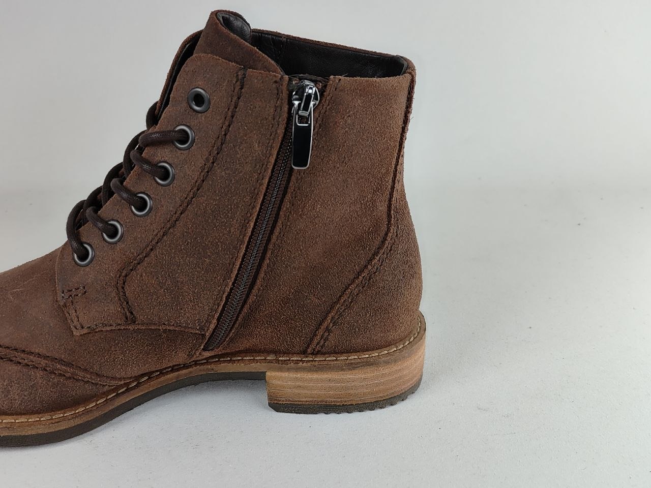A brown suede ankle boot with a side zipper, lace-up front, and stacked wooden-look heel, shown against a light gray background.