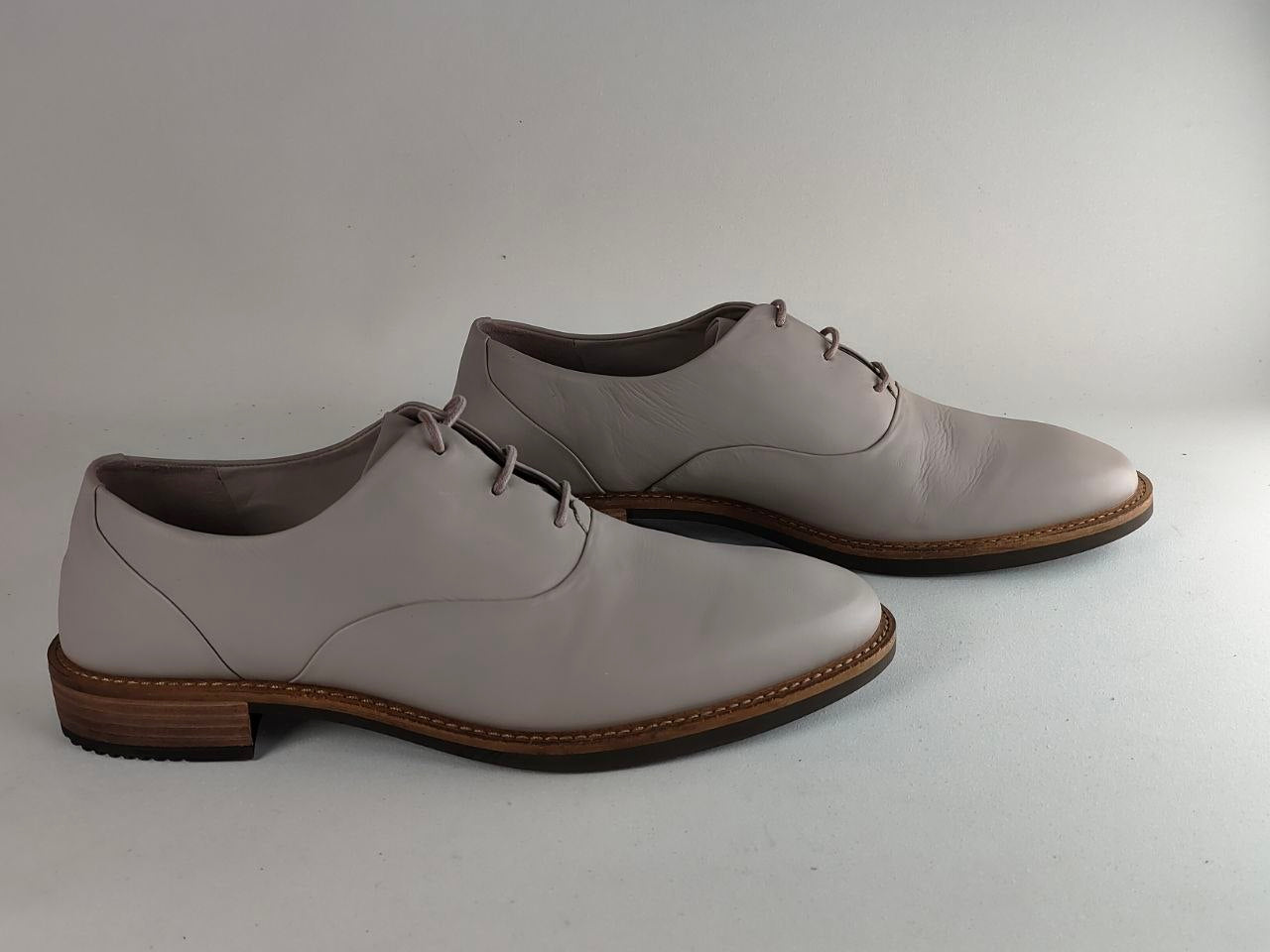 A pair of men's light gray leather oxford shoes with brown stacked heels and soles, displayed on a light gray background.