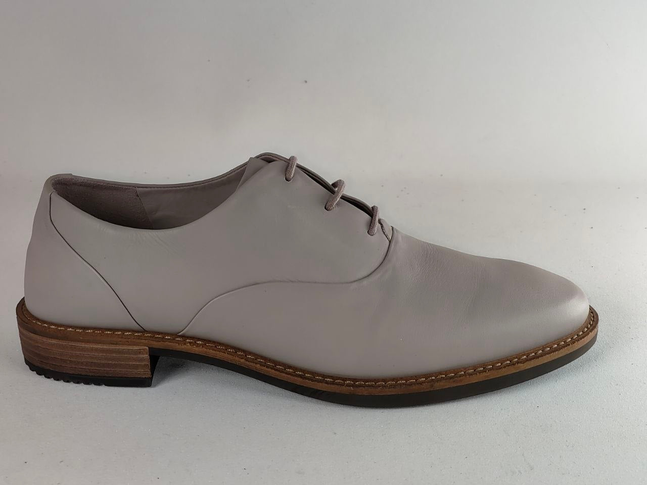A light gray leather lace-up dress shoe with a brown stacked heel and welt, shown in a side profile against a plain light gray background.