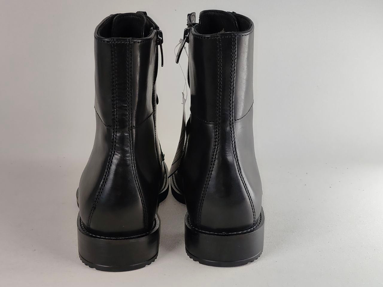 A pair of black leather ankle boots with side zippers, shown from the back against a light gray background.
