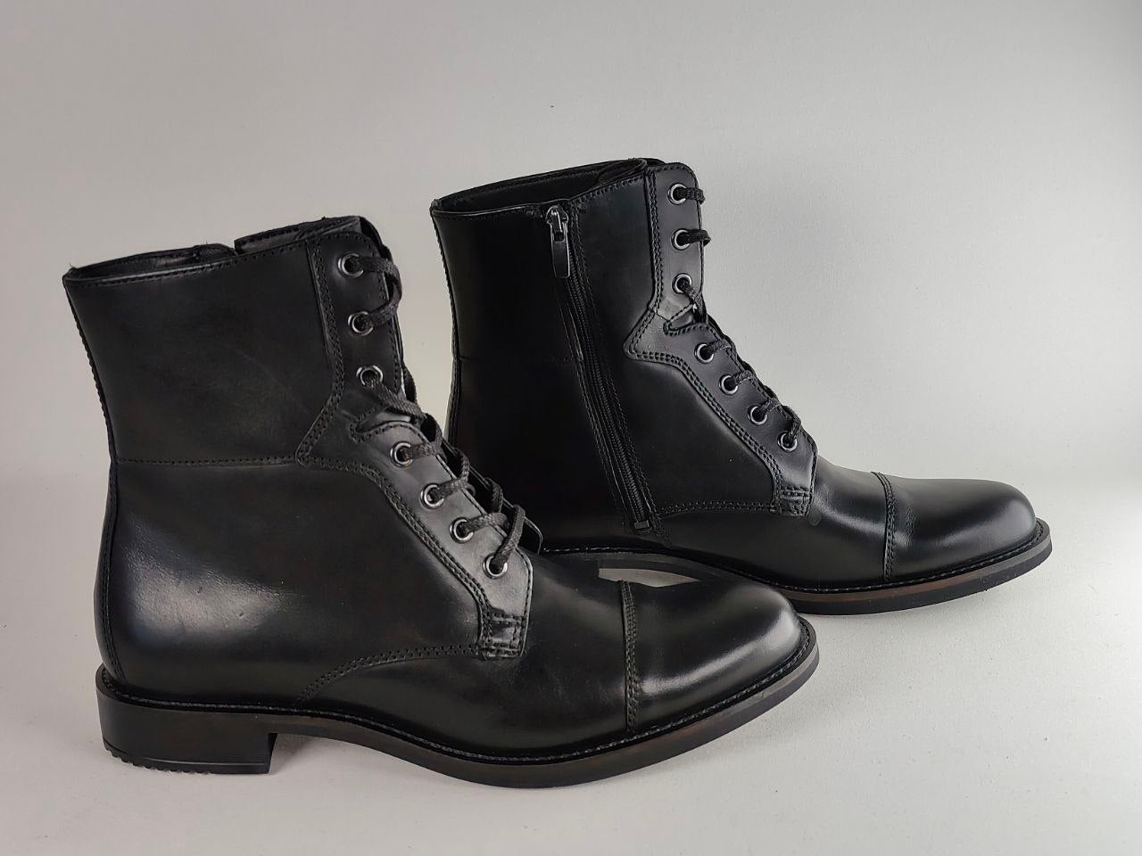 A pair of black leather lace-up ankle boots with side zippers, shown on a light gray studio background.