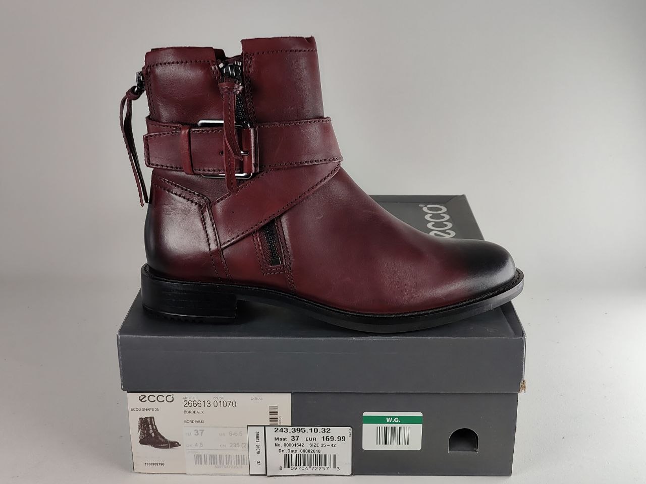 A dark burgundy leather ankle boot with side zippers and buckle straps, displayed on top of its dark gray ECCO shoebox against a neutral gray background.