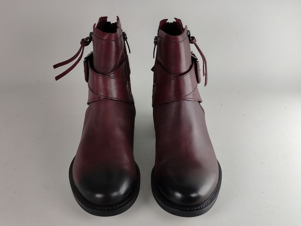 A pair of dark burgundy leather ankle boots with black rubber toe caps and side zippers, shown against a plain light gray background.
