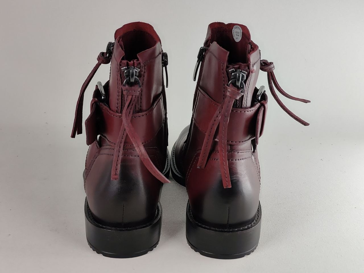 A pair of dark burgundy leather ankle boots with black soles, shown from the back against a light gray background.