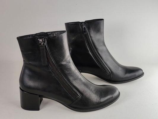 A pair of black leather ankle boots with side zippers and block heels, photographed on a neutral light gray background.