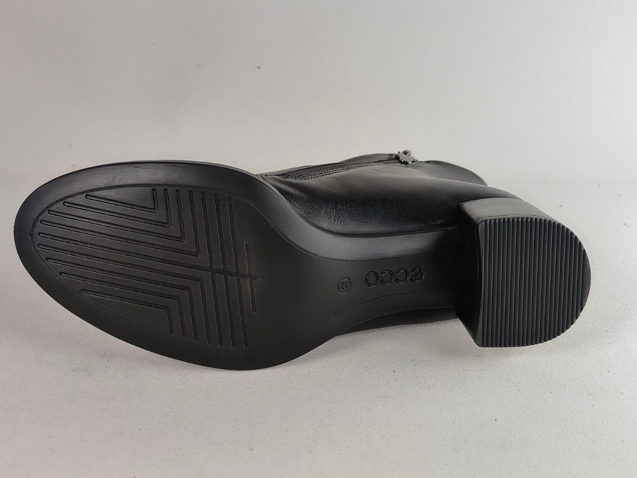 The outsole of a black leather boot by ECCO, showing the tread pattern and brand name embossed on the heel, photographed against a light gray background.