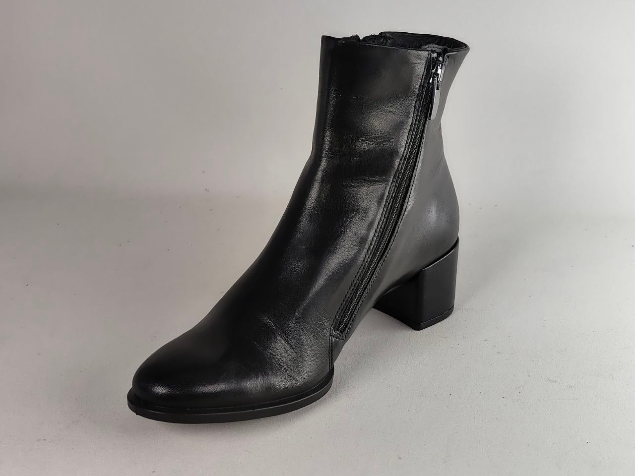 A single black leather ankle boot with a low block heel and side zipper, photographed on a neutral light gray background.