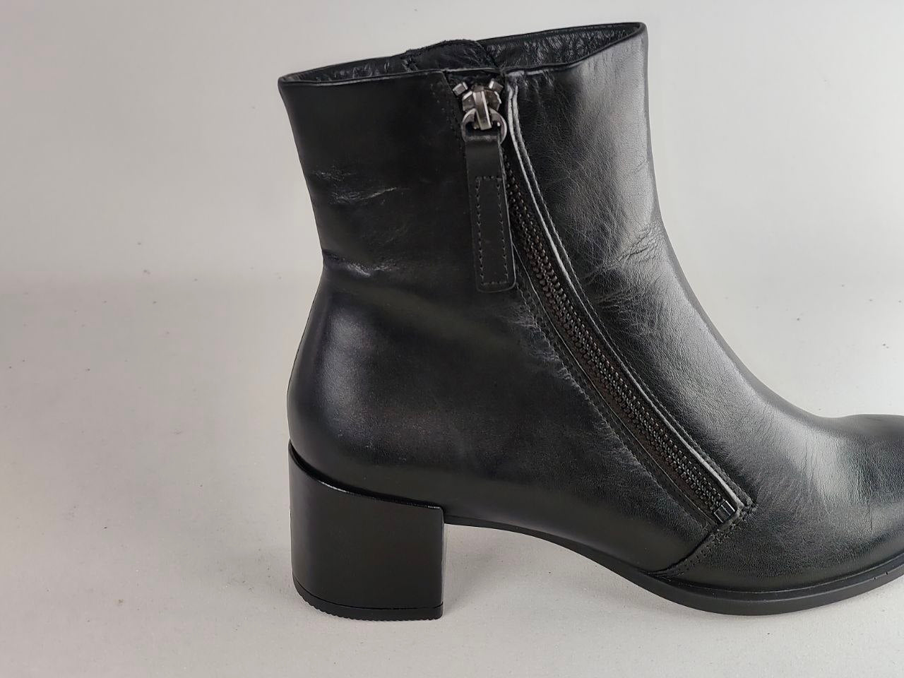 A black leather ankle boot with a side zipper and a chunky block heel, shown from a side profile view against a light gray background.