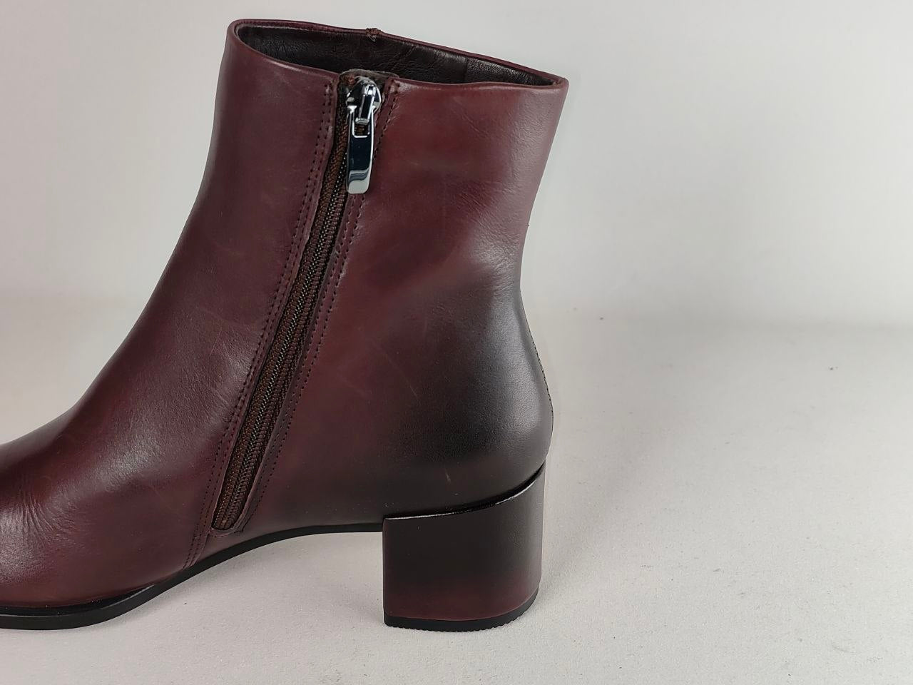 A dark burgundy leather ankle boot with a side zipper and a low block heel, shown from a side profile view against a light gray background.