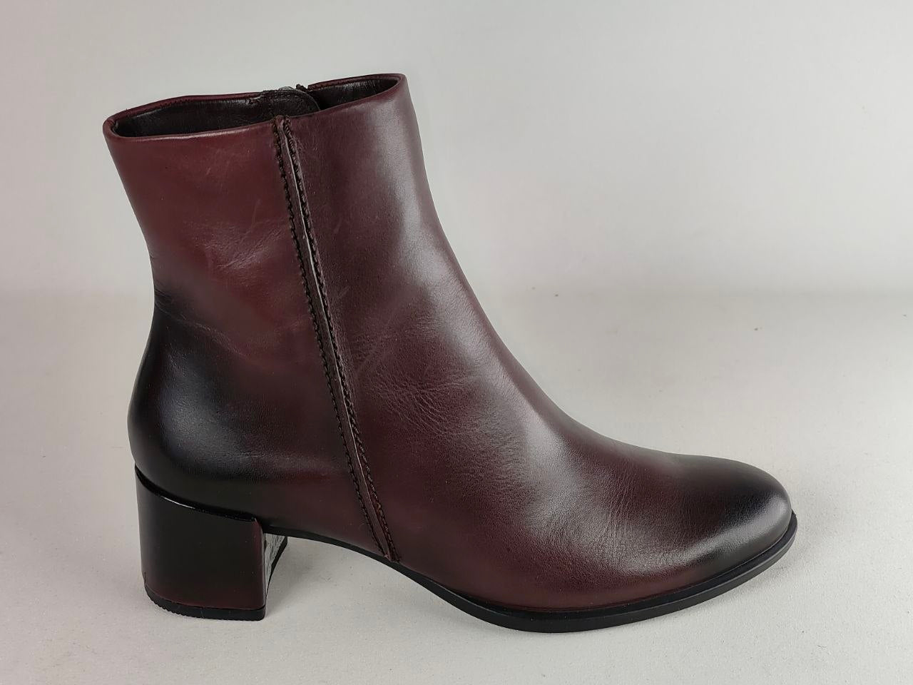 A dark burgundy leather ankle boot with a low block heel, shown from a side profile against a neutral light gray background.