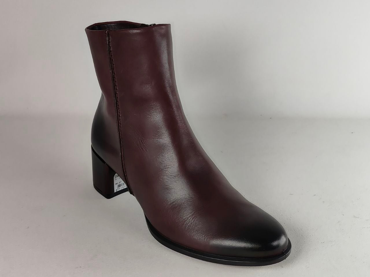 A dark brown leather ankle boot with a low block heel and a pointed toe, photographed against a neutral light gray background.