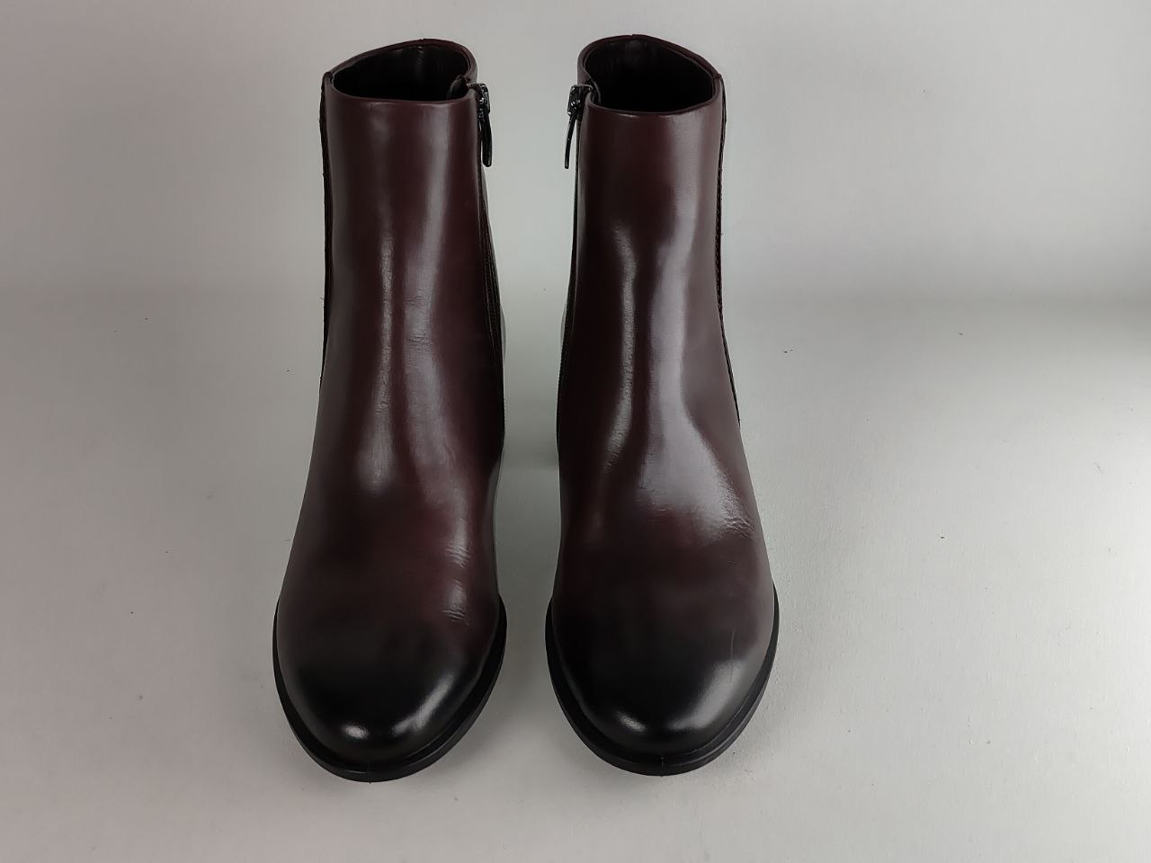A pair of dark burgundy leather ankle boots with black toes and heels, shown from the front on a light gray background.