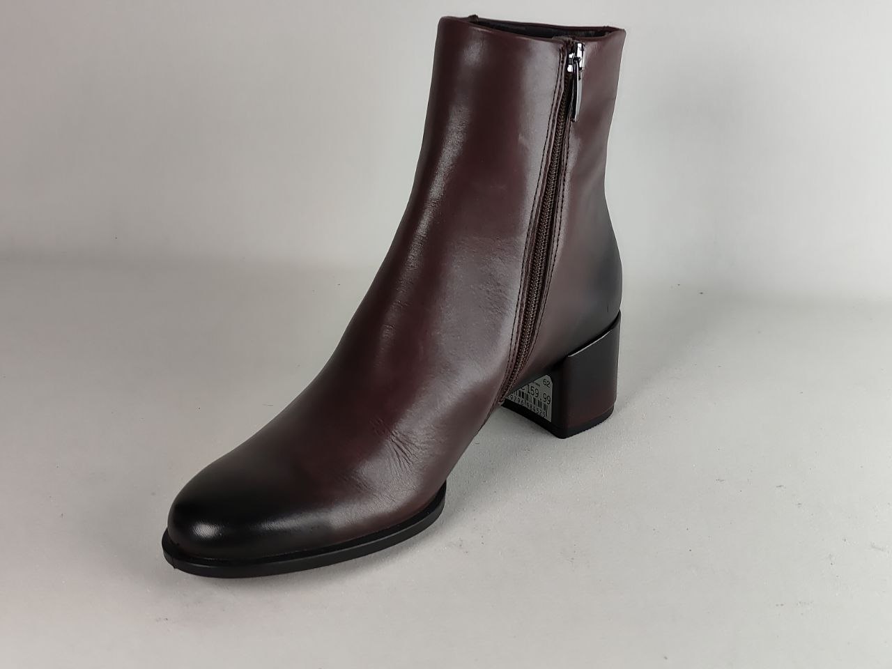 A dark brown leather ankle boot with a side zipper, low block heel, and rounded toe, photographed on a neutral light gray background.