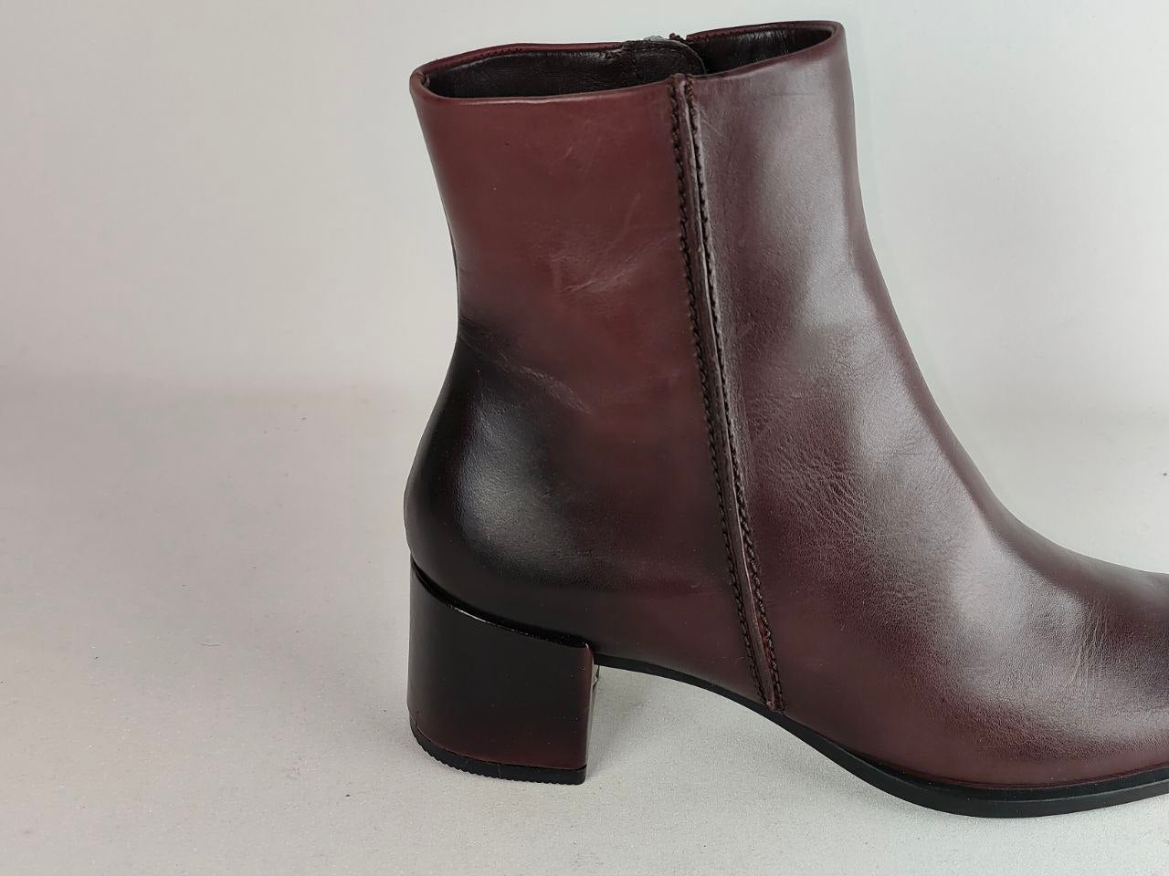 A dark brown leather ankle boot with a low block heel, shown from a side profile view against a neutral light gray background.