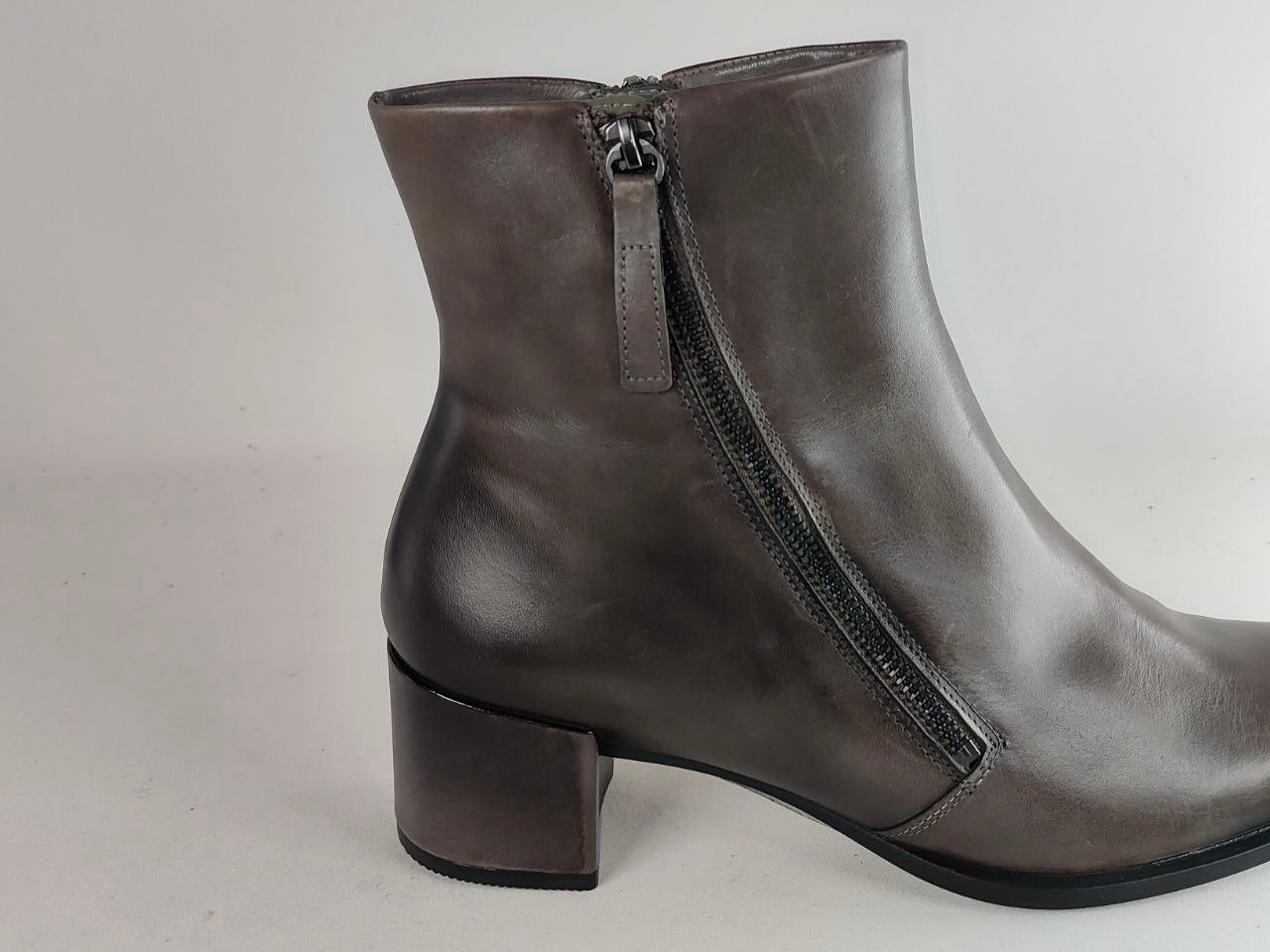 A dark gray leather ankle boot with a low block heel and a side zipper, shown from a side profile view against a light gray background.