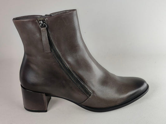 A dark brown leather ankle boot with a side zipper, low block heel, and rounded toe, shown against a neutral light gray background.