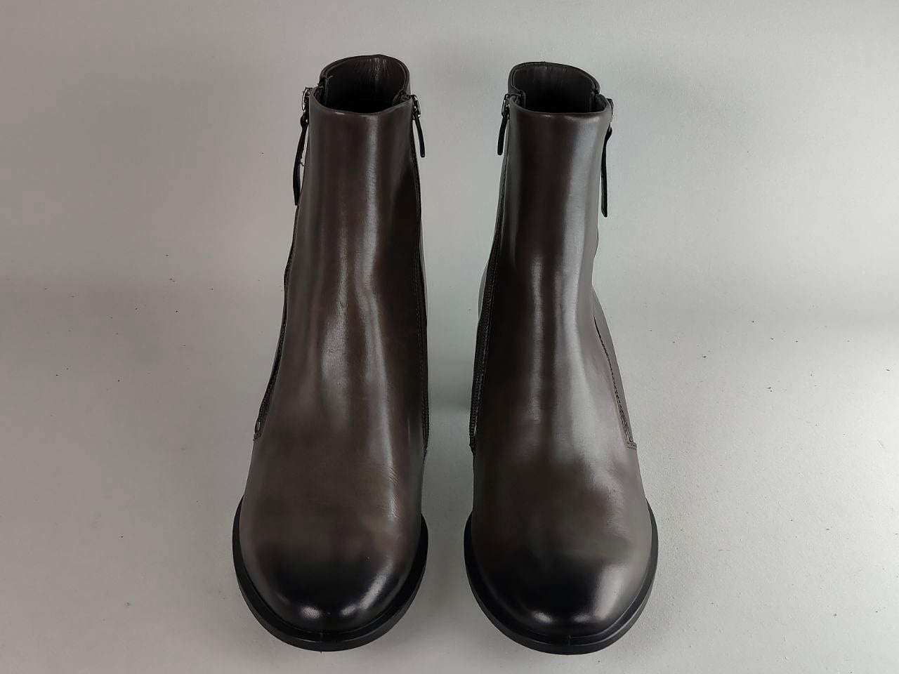 A pair of dark brown leather ankle boots with side zippers, shown from a front-facing perspective on a neutral light gray background.