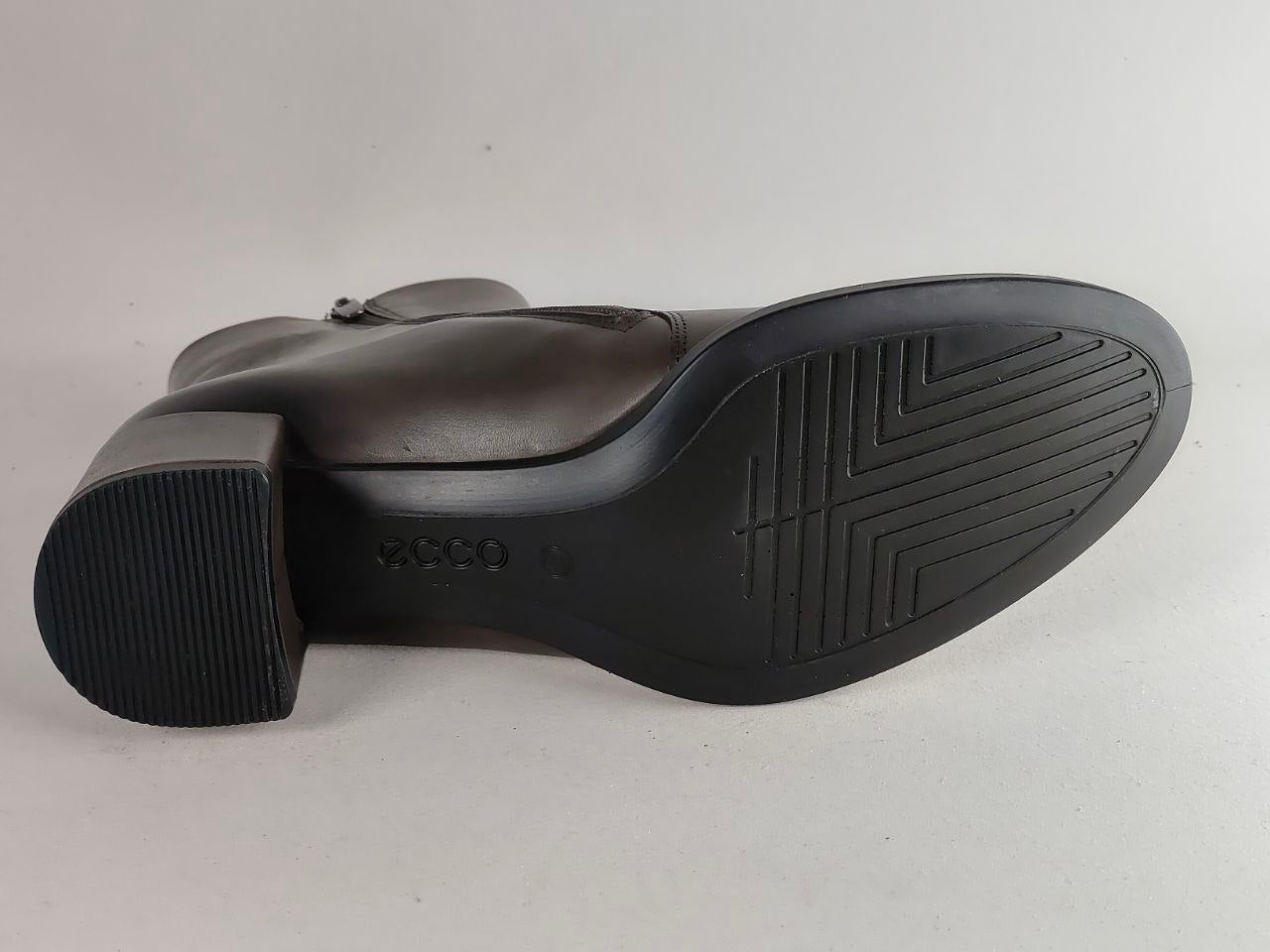 A close-up view of the black rubber outsole of a boot, showing the tread pattern and embossed 'ecco' brand name, on a light gray background.