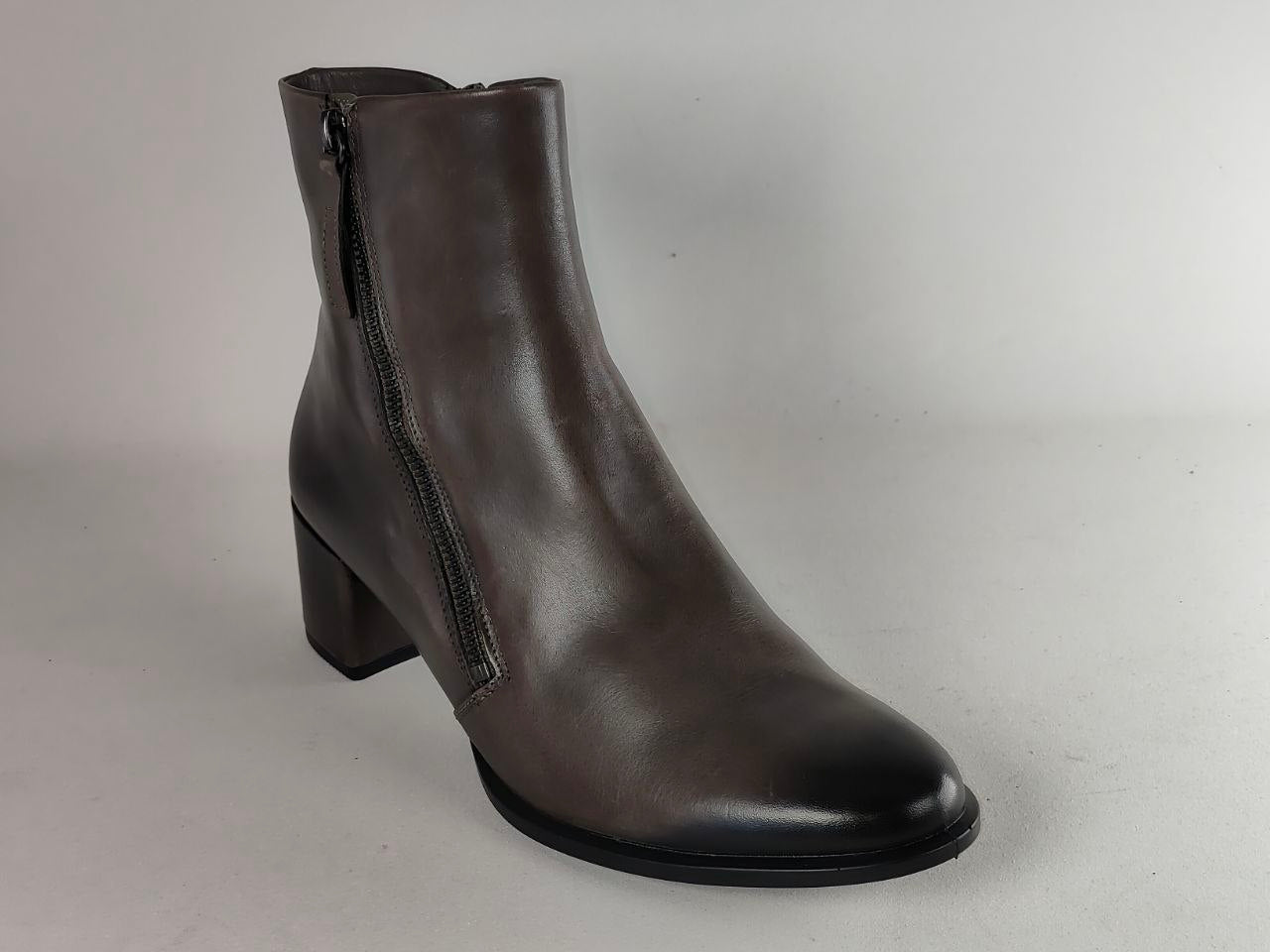 A dark brown leather ankle boot with a side zipper, block heel, and rounded toe, photographed against a neutral light gray background.