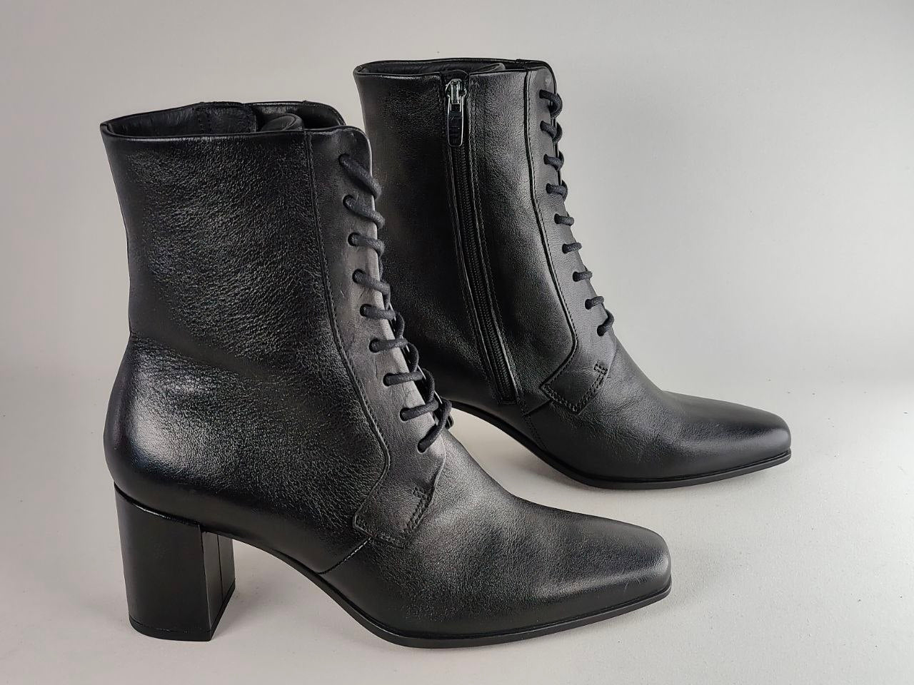 A pair of black leather lace-up ankle boots with a block heel, shown on a neutral light gray background.