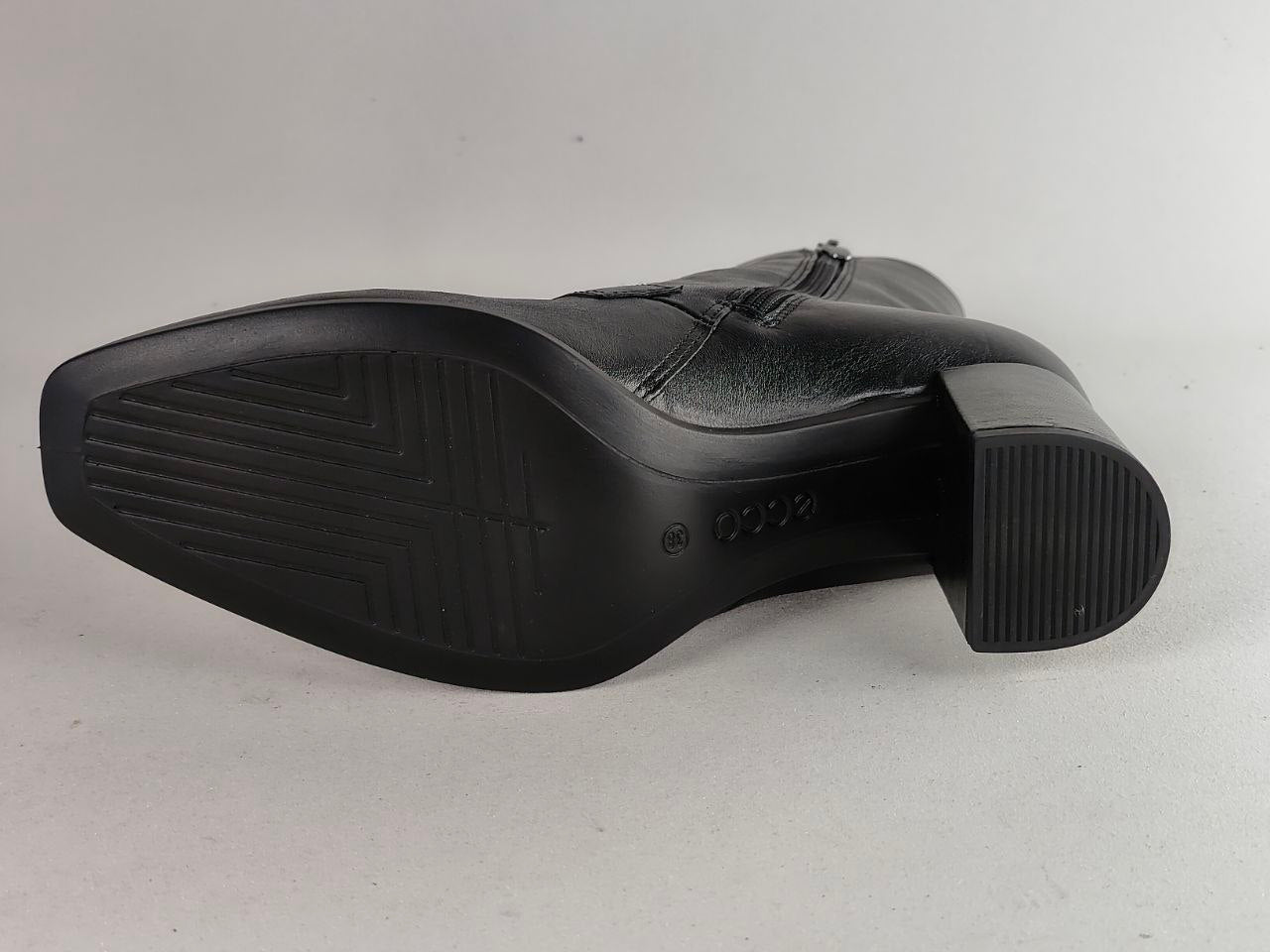 A black leather boot shown from the sole side, featuring a low block heel and a textured treaded outsole, photographed against a neutral light gray background.