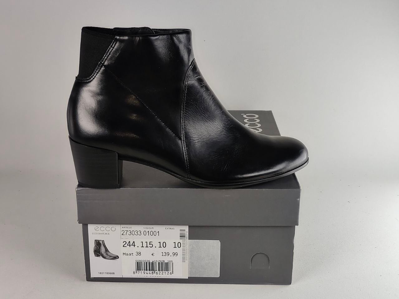 A black leather ankle boot with a block heel, displayed on top of its gray Eccos shoebox against a light gray background.