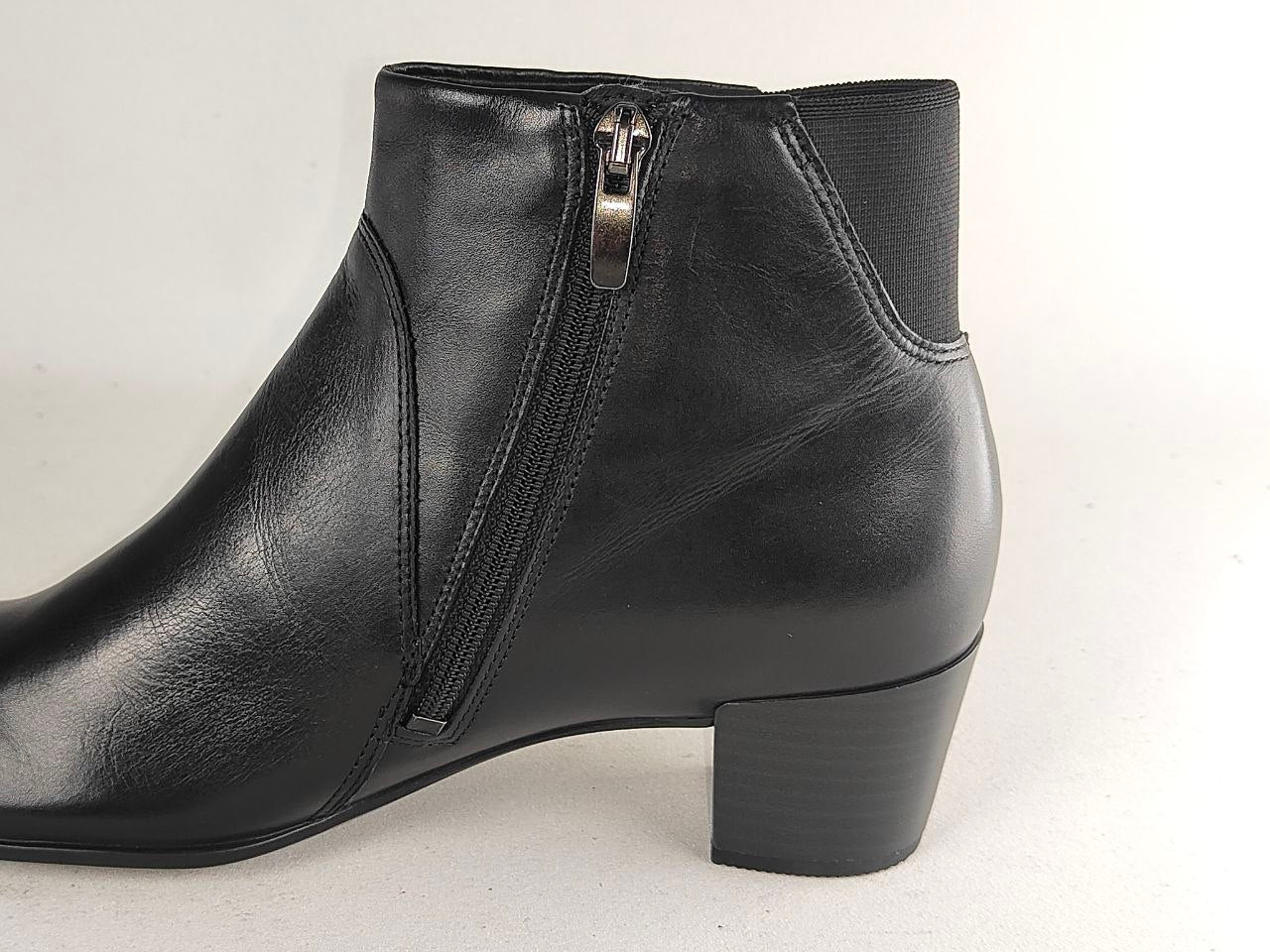 A black leather ankle boot with a side zipper, block heel, and elastic side panel, shown from a side profile view against a light gray background.