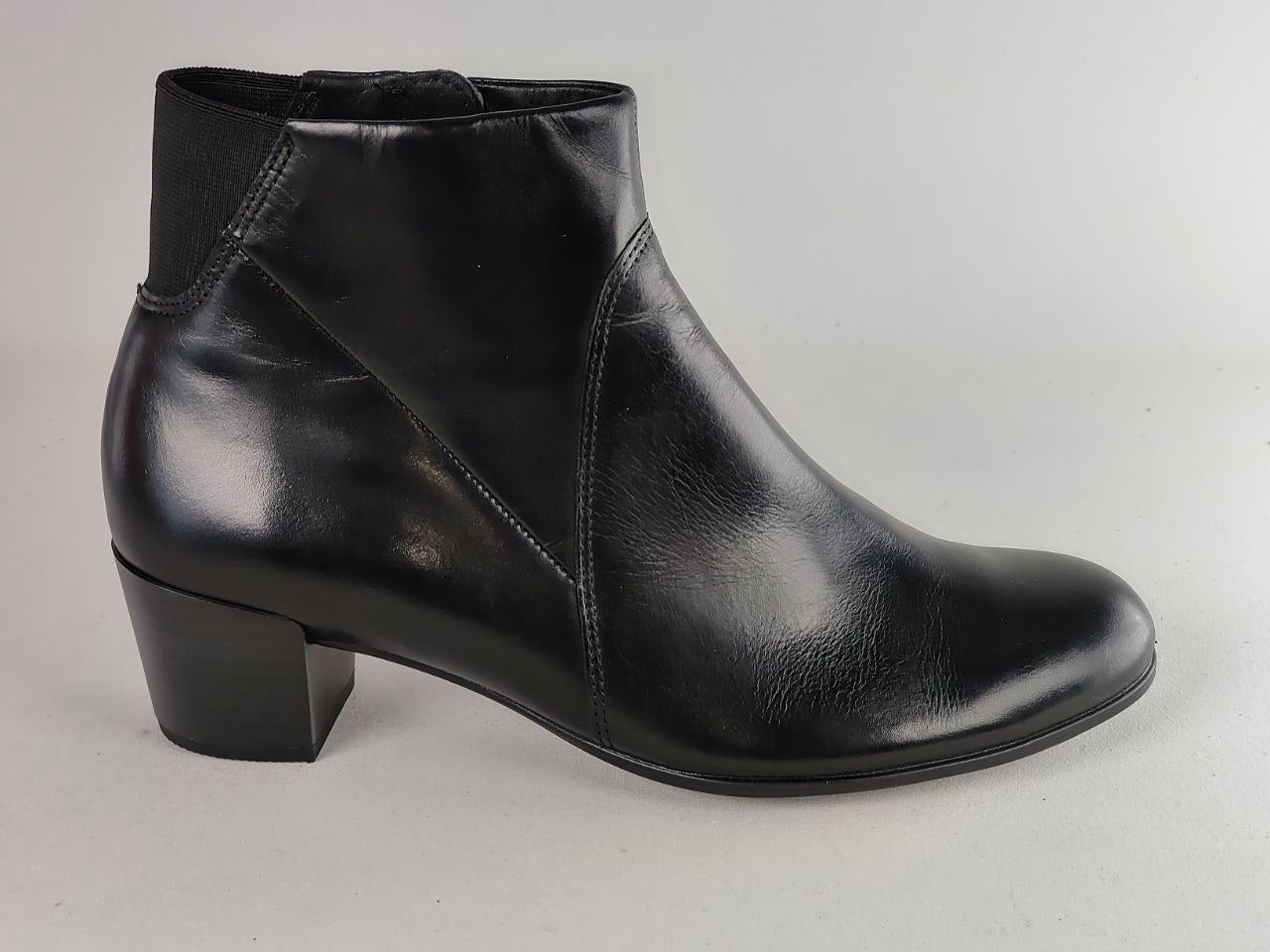 A black leather ankle boot with a low block heel and elastic side panels, shown from a side profile against a neutral light gray background.