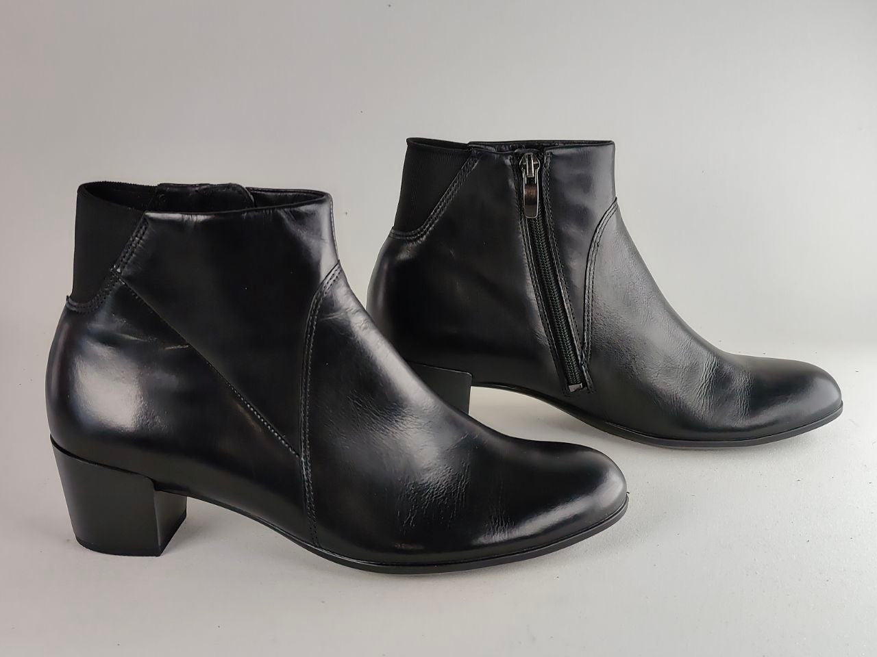 A pair of black leather ankle boots with low block heels, shown from the side and back on a light gray background.