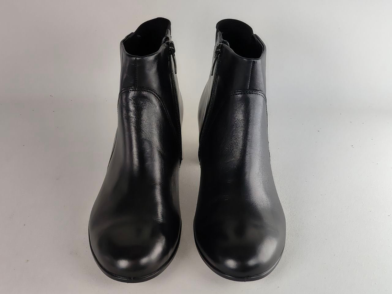 A pair of black leather ankle boots with side zippers, shown from a front-facing perspective on a light gray background.