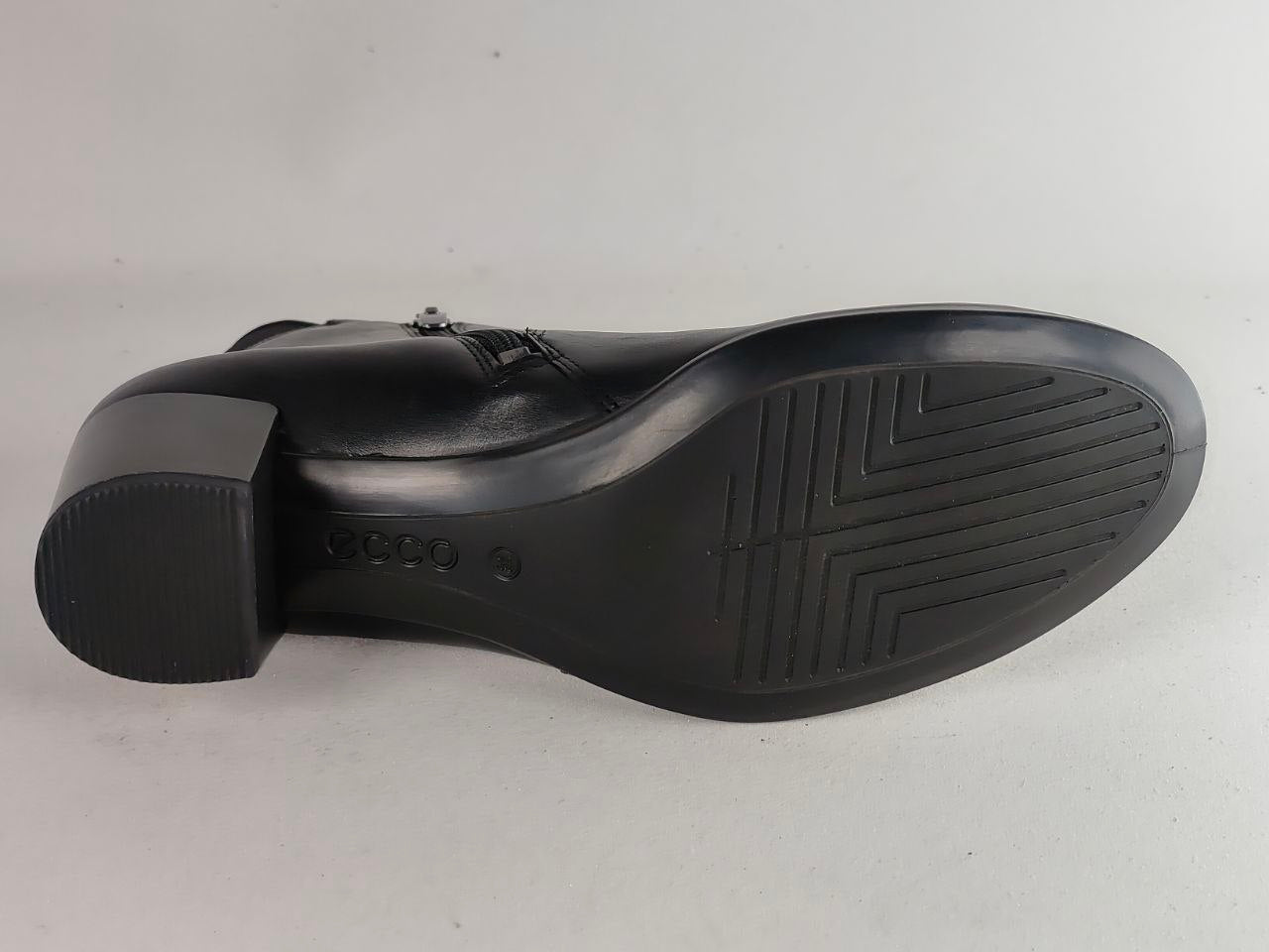 A black leather dress boot shown from a side profile view, displaying its sole with tread patterns and a low block heel, set against a plain light gray background.
