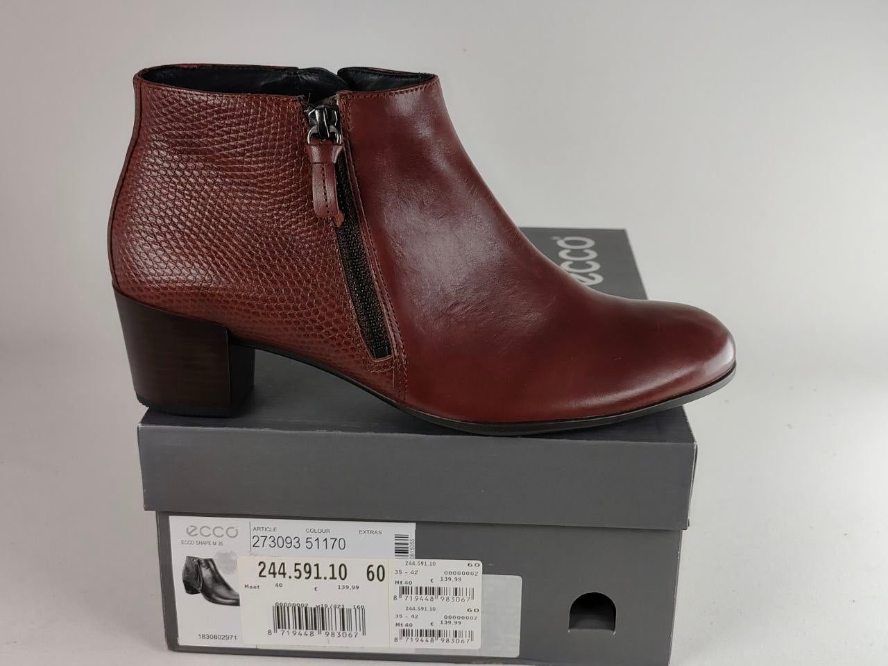A single brown leather ankle boot with a textured side panel, black zipper, and block heel, displayed on top of a gray ECCO shoebox against a light gray background.