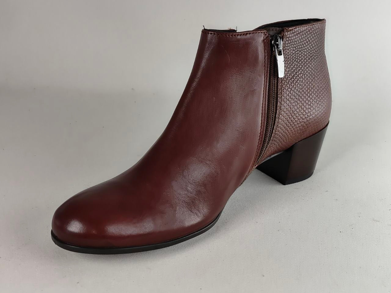 A single women's ankle boot in a deep burgundy brown, featuring a smooth leather front and a textured snakeskin-patterned side panel with a visible silver zipper.