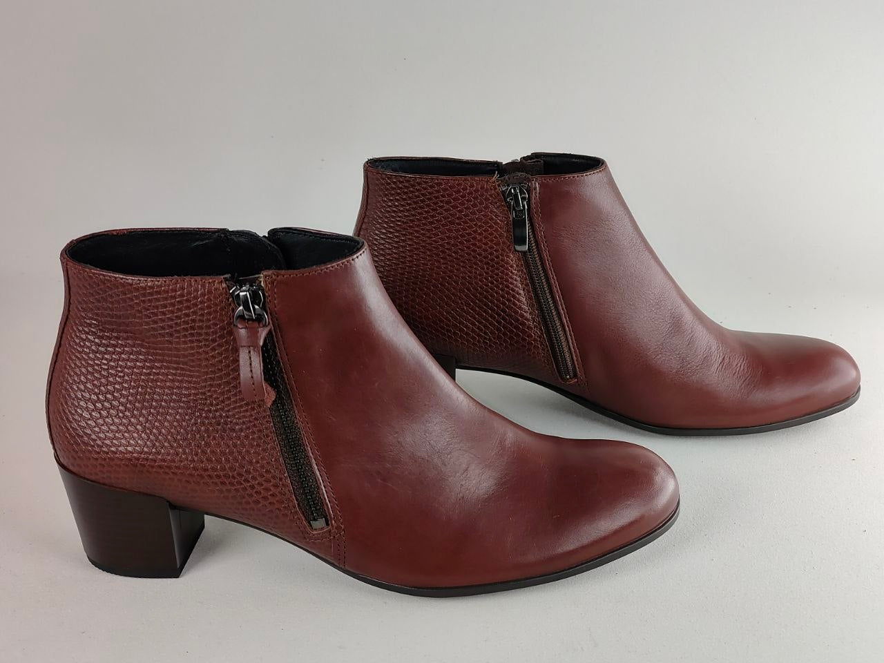 A pair of women's brown leather ankle boots with a side zipper, low block heel, and textured pattern on the outer side, shown against a neutral light gray background.