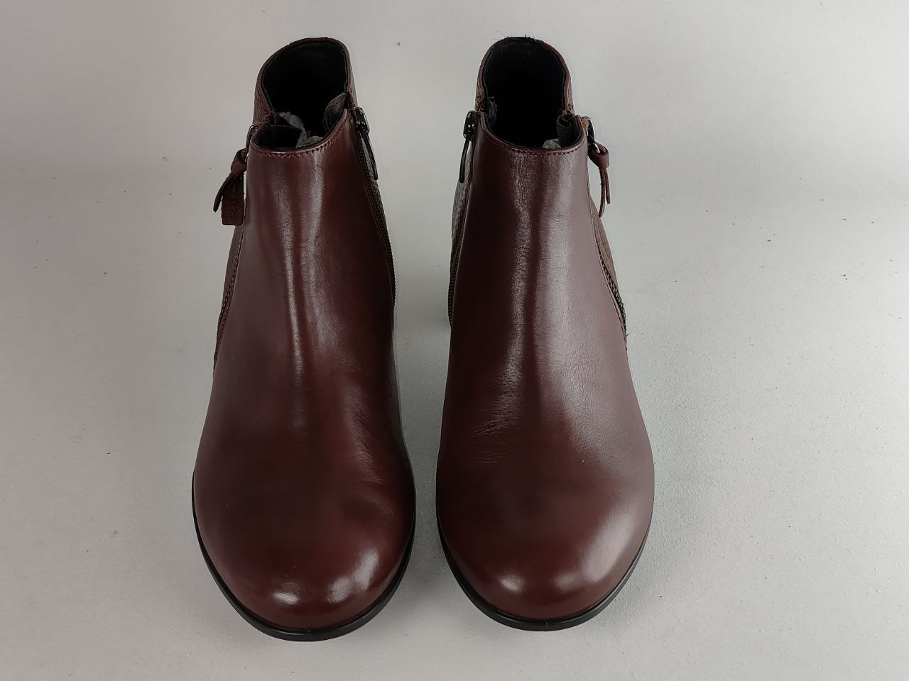 A pair of dark brown leather ankle boots with side zippers and small side tabs, shown from the front on a light gray background.