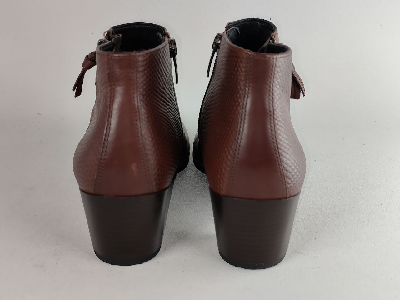 A pair of women's brown leather ankle boots with a textured pattern, low block heels, and side ties, shown from the back on a light gray background.