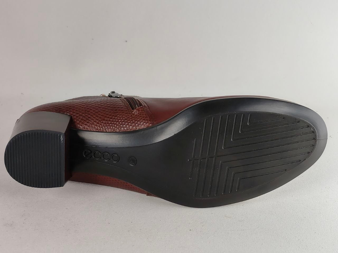 A close-up bottom view of a men's dress shoe showing the brown textured leather vamp and a black rubber outsole on a light gray background.