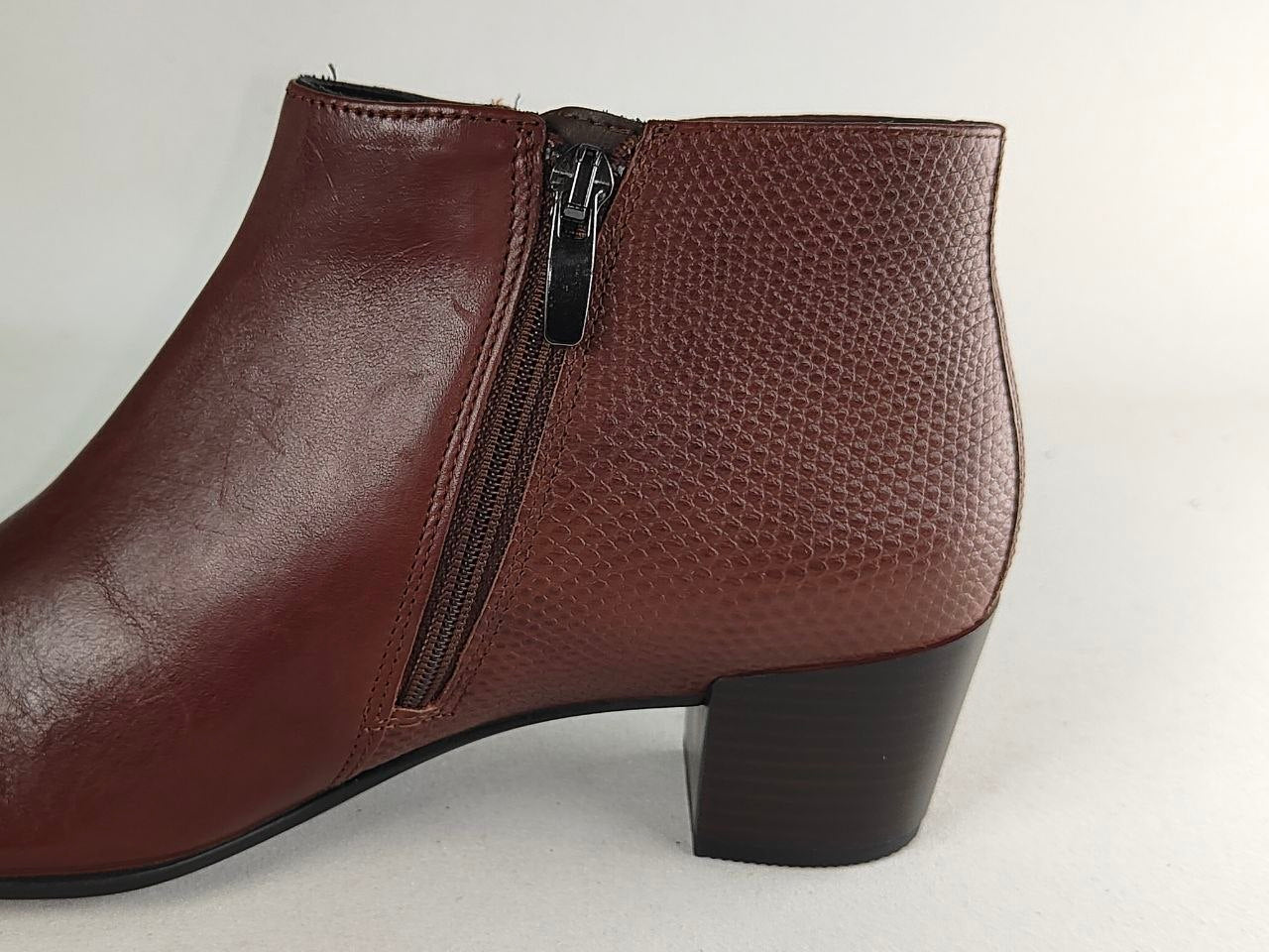 A brown leather ankle boot with a side zipper, featuring a textured pattern on the upper and a low block heel, shown against a plain light background.