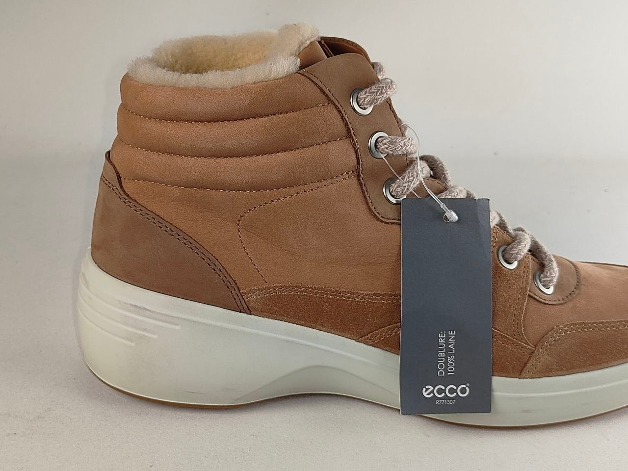A tan suede high-top sneaker boot with a cream shearling lining, featuring a white sole and a dark gray ECCO brand tag attached to the laces.