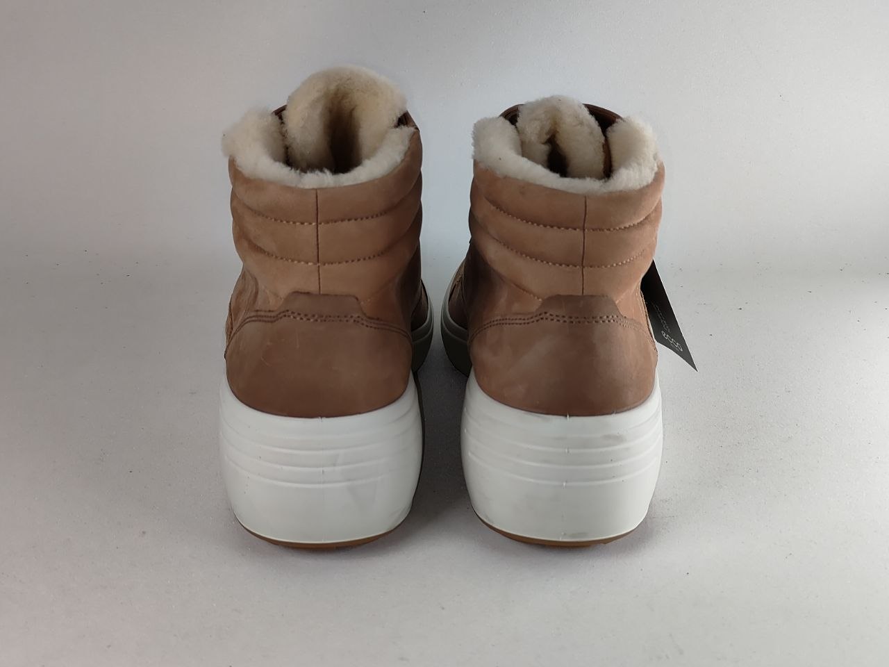 A pair of brown suede high-top winter boots with fluffy cream shearling lining and thick white platform soles, shown from the back against a plain light gray background.