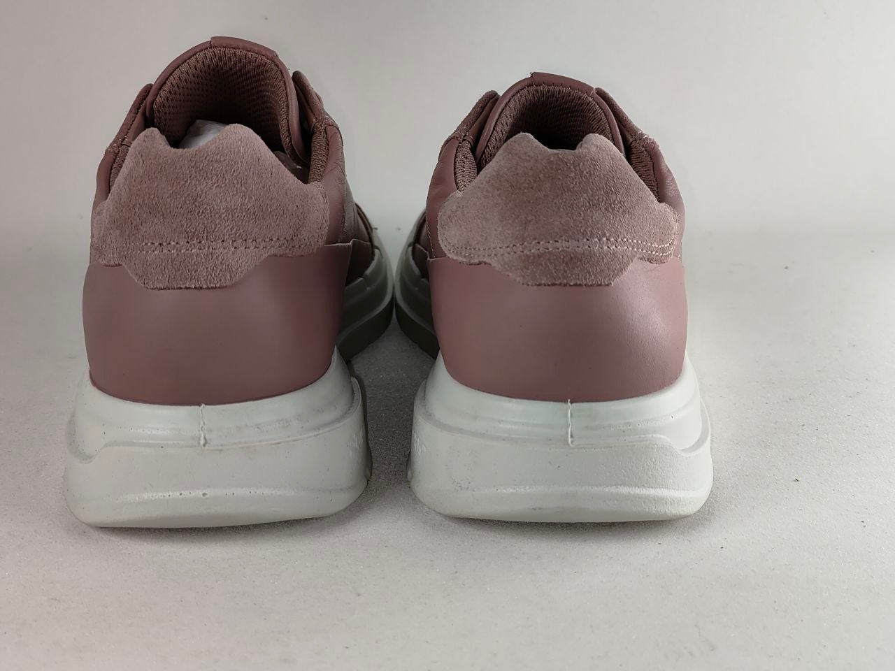 A pair of women's low-top sneakers shown from the back, featuring dusty rose suede and smooth leather panels with chunky white platform soles.