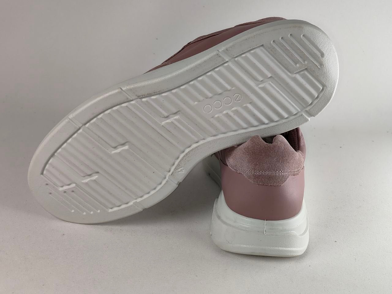 A pair of low-top sneakers shown from the side, with one shoe tilted to display its white textured sole. The upper is a dusty mauve or muted rose color, and the sole is white.