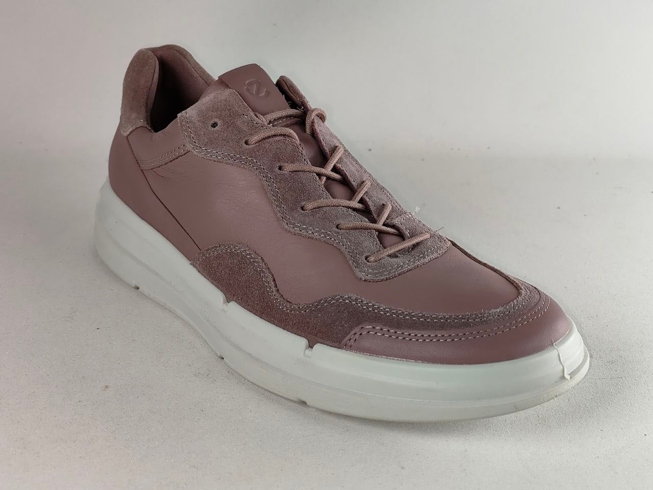 A single low-top sneaker in a dusty mauve-brown color, featuring a mix of smooth leather and suede panels, matching laces, and a thick white platform sole, photographed on a neutral light gray background.