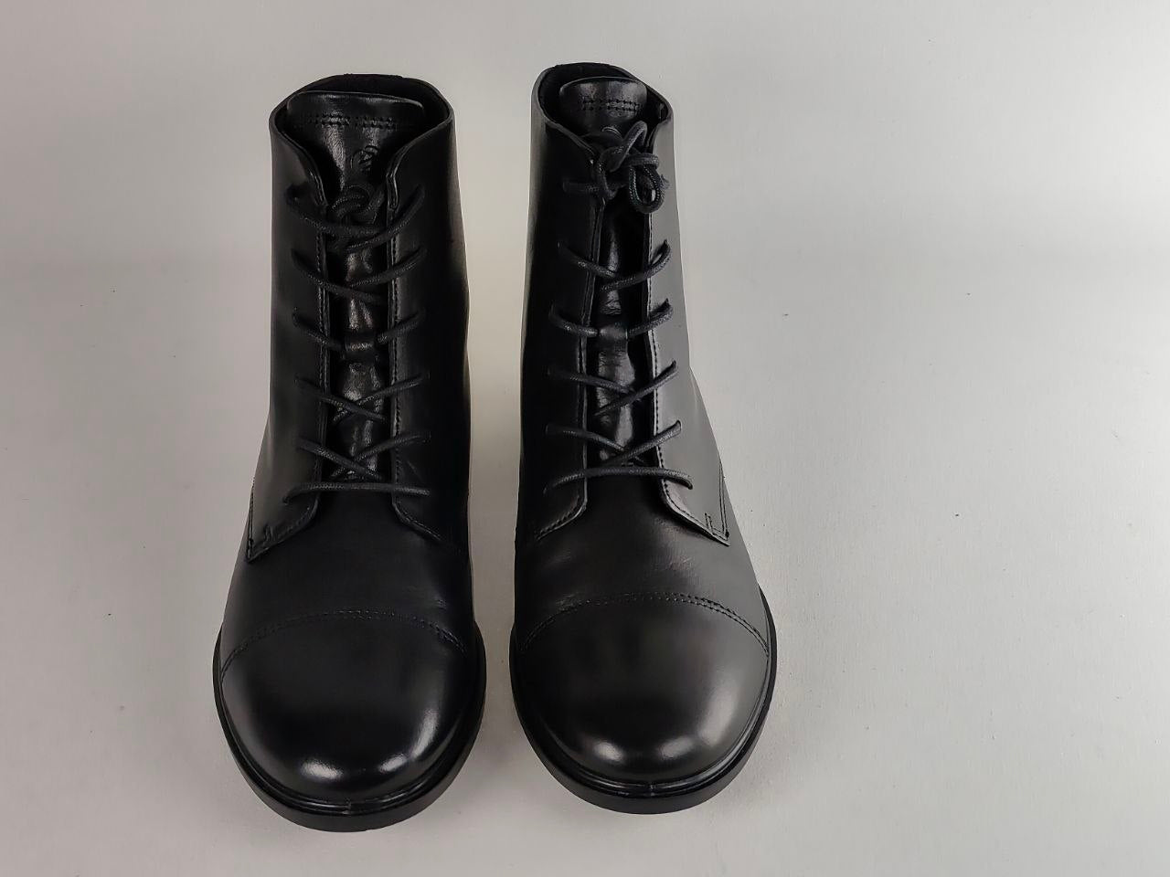 A pair of black leather lace-up ankle boots photographed from the front on a plain light gray studio background.